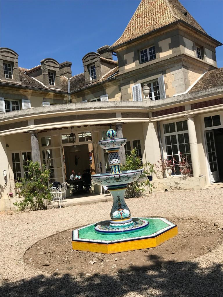 Decorative fountain in front of a large house with a clear blue sky.