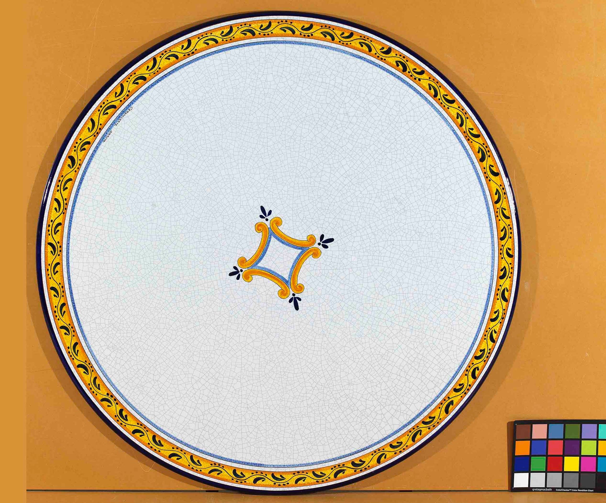 Birds eye view of the hand-painted Italian ceramic glaze Palermo Classico central ochre cartouche and yellow scroll border on a round volcanic stone tabletop