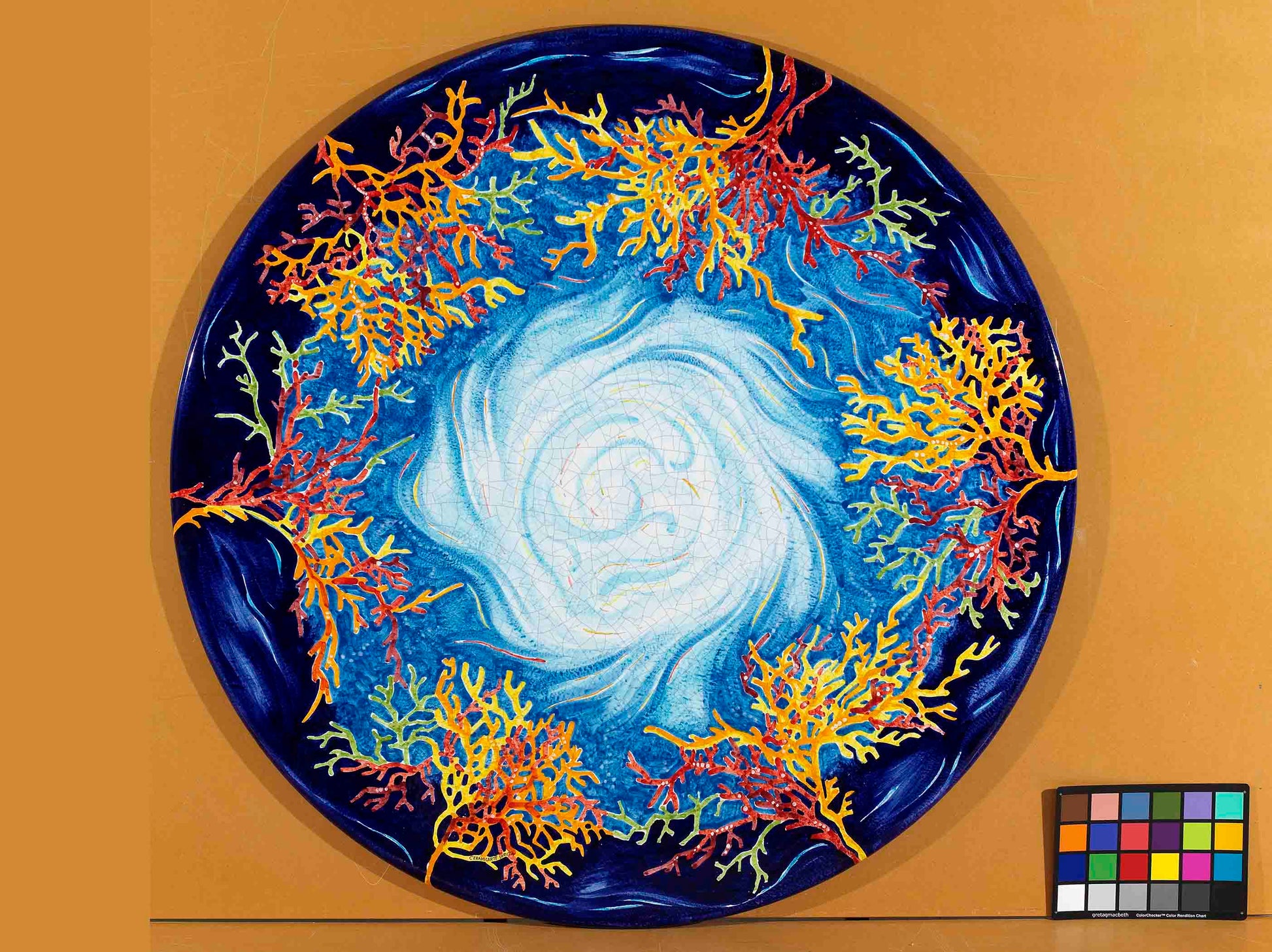 Birds eye view of the hand-painted Italian ceramic glaze Panarea Oceanico central turquoise vortex and colorful coral branch border on a round volcanic stone tabletop