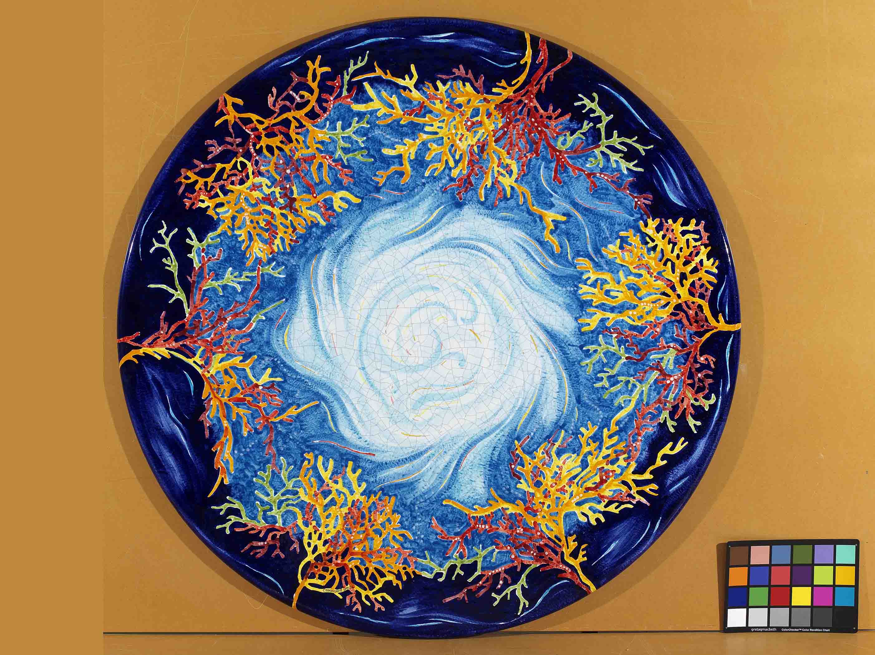 Birds eye view of the hand-painted Italian ceramic glaze Panarea Oceanico central turquoise vortex and colorful coral branch border on a round volcanic stone tabletop