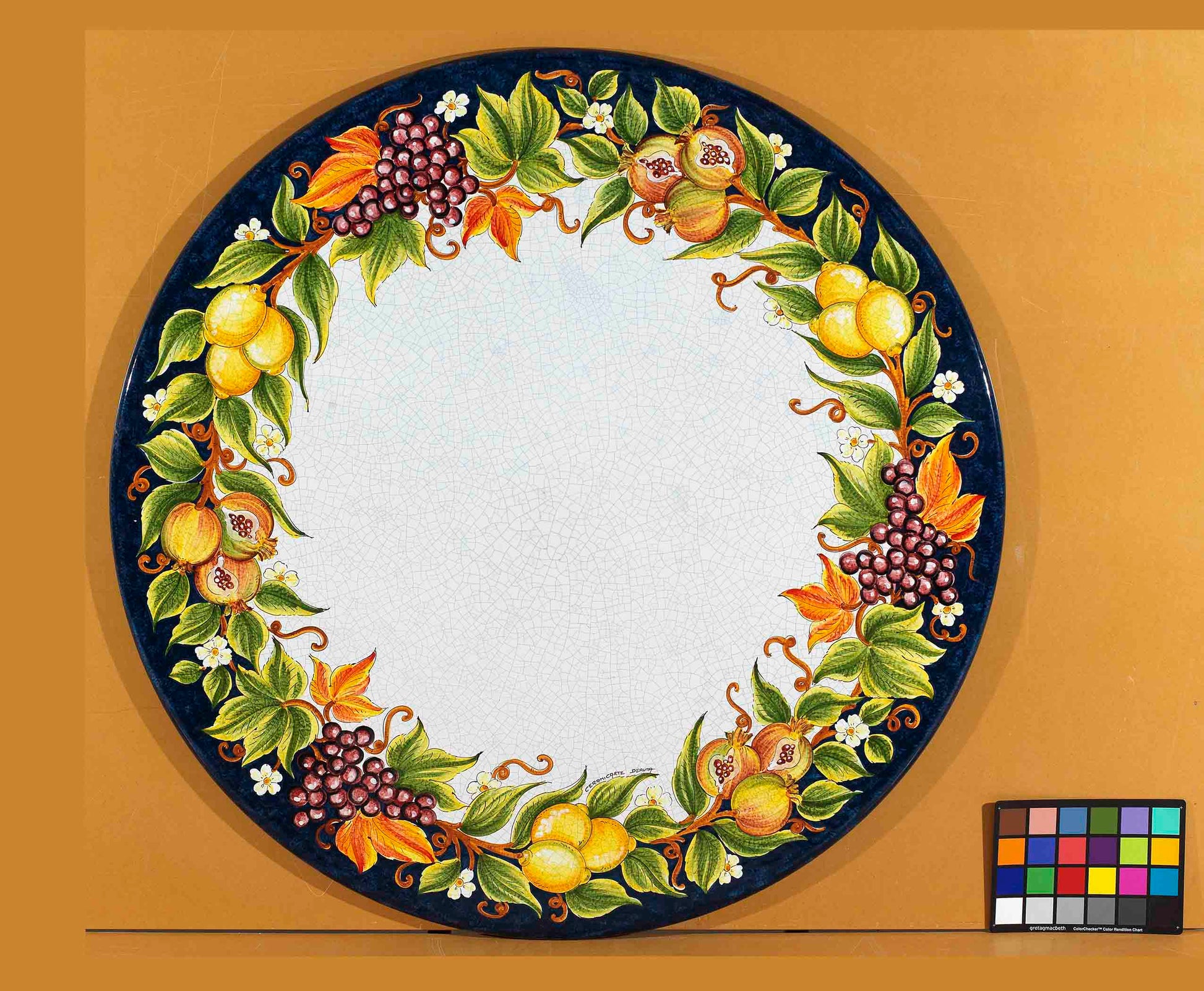 Birds eye view of the hand-painted Italian ceramic glaze Ravello Frutteto lemons, grapes, and pomegranate wreath on a round volcanic stone tabletop