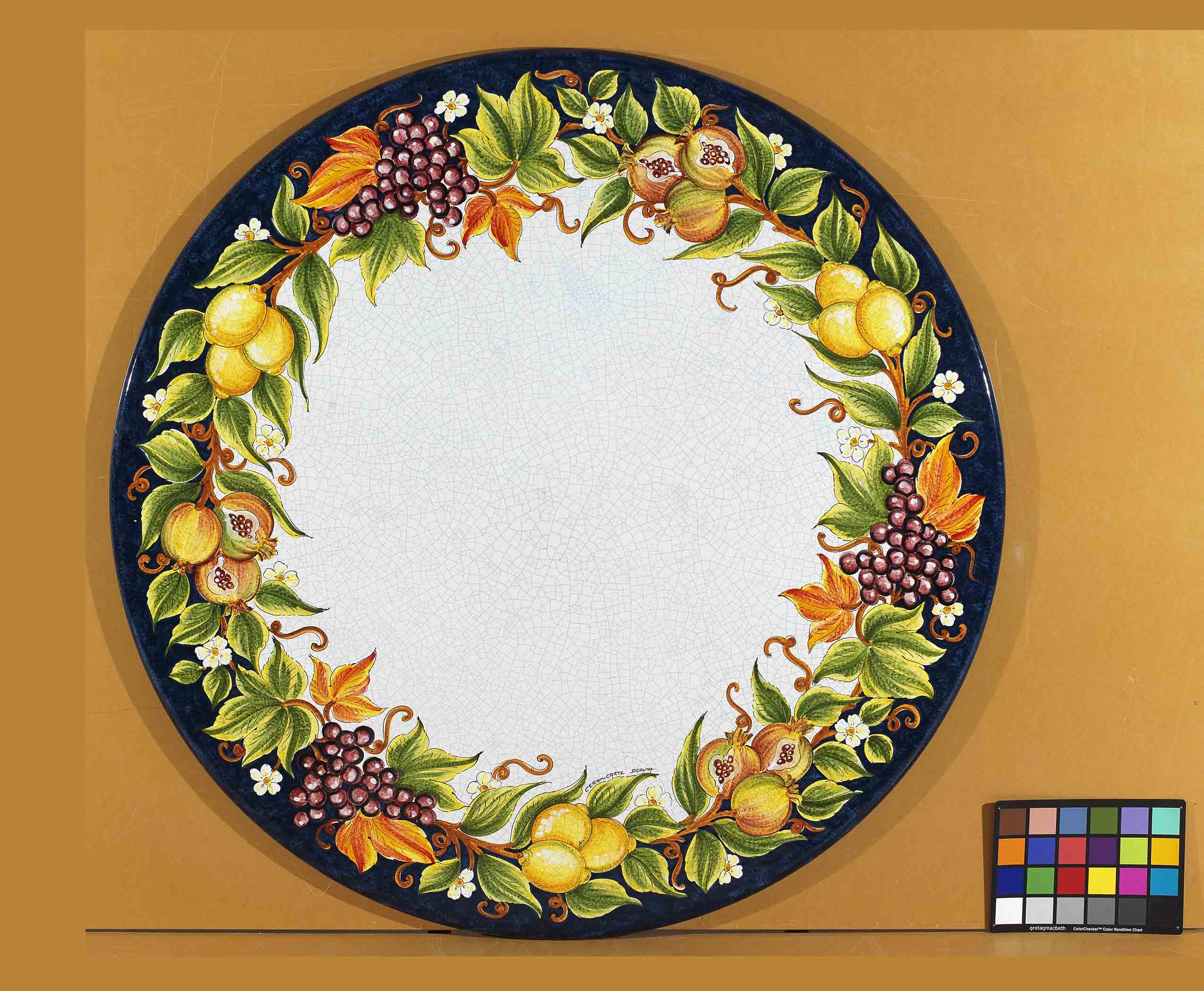 Birds eye view of the hand-painted Italian ceramic glaze Ravello Frutteto lemons, grapes, and pomegranate wreath on a round volcanic stone tabletop