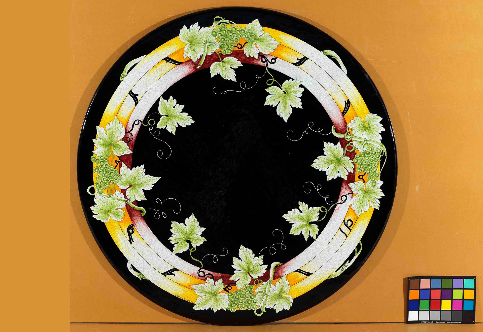 Birds eye view of the hand-painted Italian ceramic glaze Chianti Vigneto overlapping geometric rings and green grape clusters on a round volcanic stone tabletop