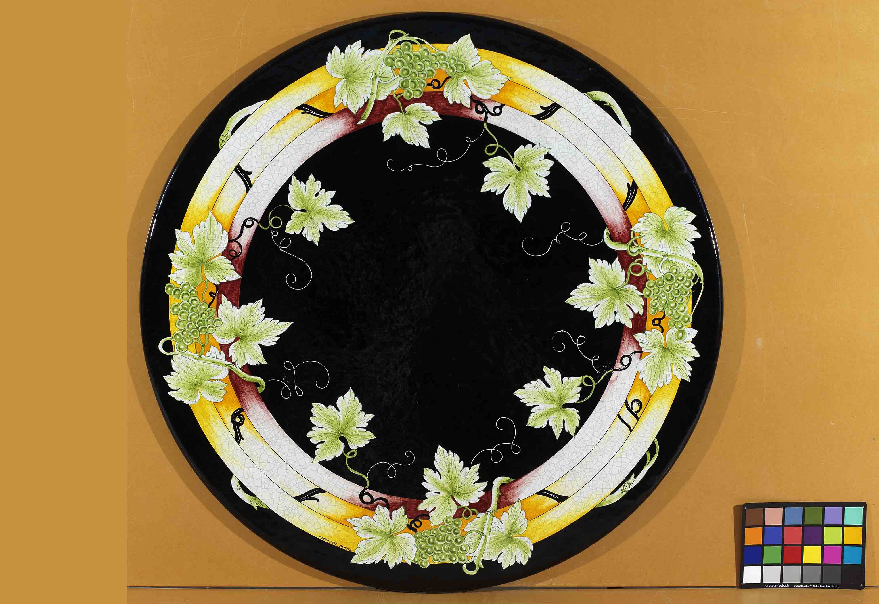 Birds eye view of the hand-painted Italian ceramic glaze Chianti Vigneto overlapping geometric rings and green grape clusters on a round volcanic stone tabletop