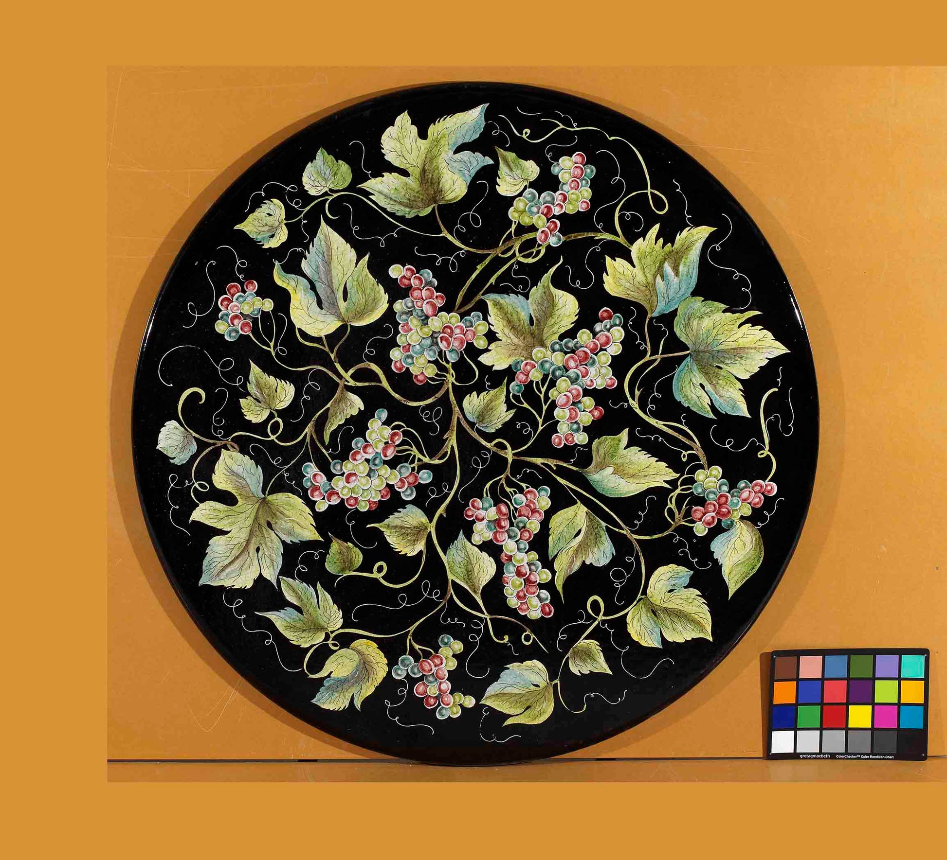 Birds eye view of the hand-painted Italian ceramic glaze Montalcino Vendemmia all-over green and purple grape cluster pattern on a round volcanic stone tabletop