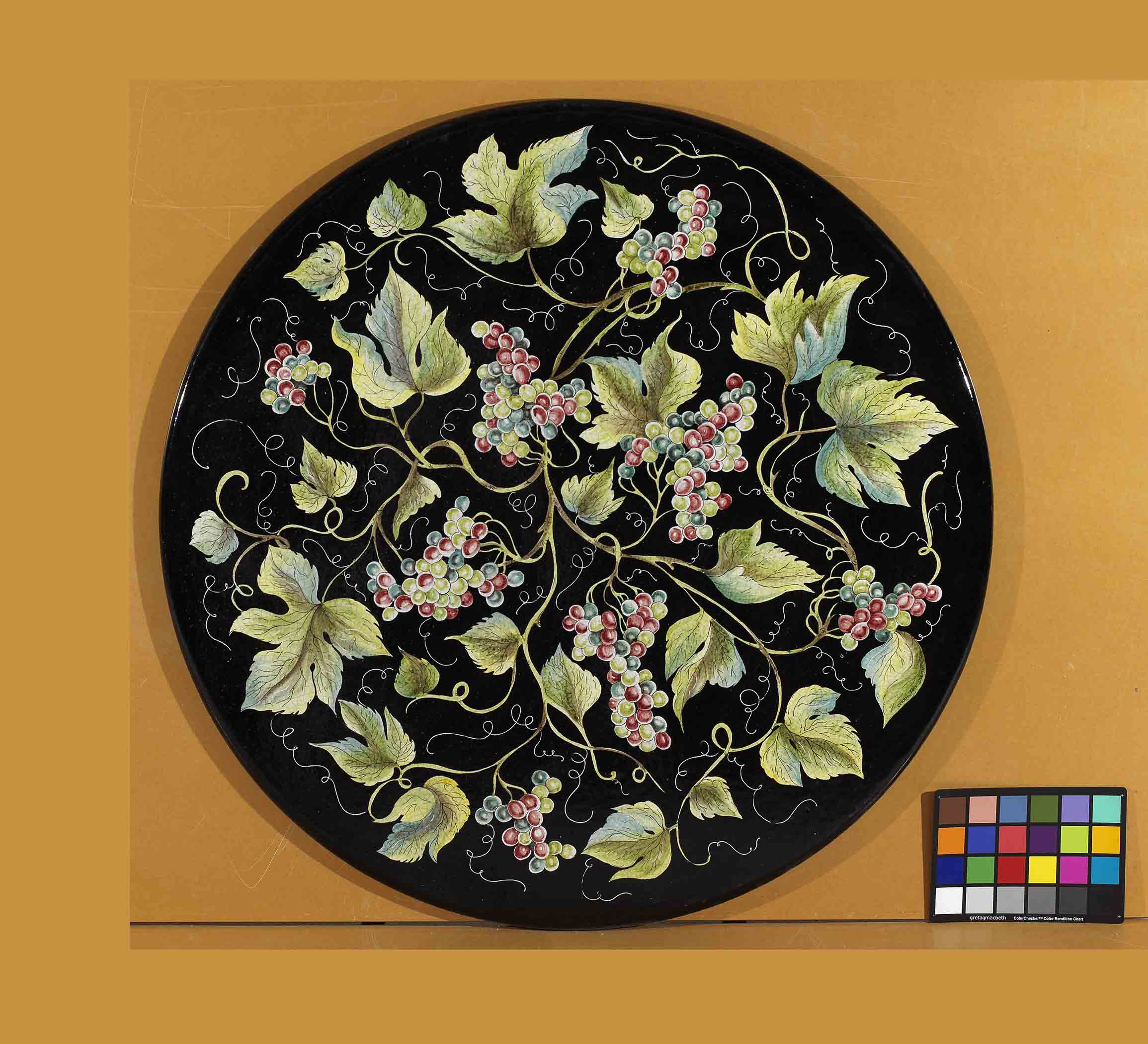 Birds eye view of the hand-painted Italian ceramic glaze Montalcino Vendemmia all-over green and purple grape cluster pattern on a round volcanic stone tabletop